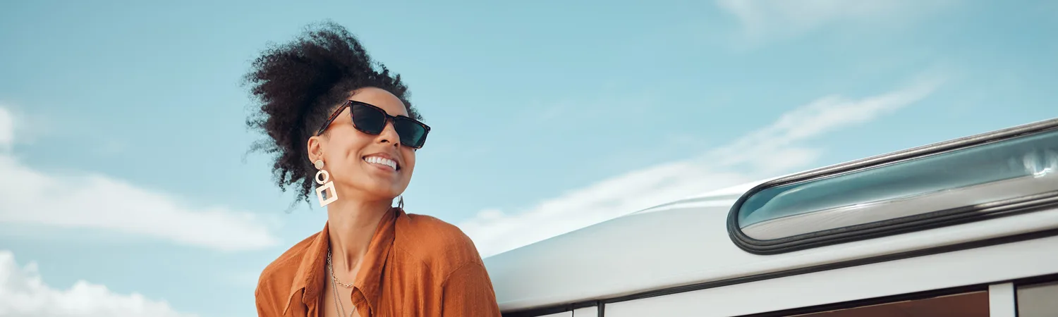 A smiling woman in sunglasses outdoors under a bright blue sky